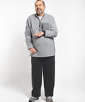 A man wearing a heather gray quarter-zip fleece pullover, black sweatpants, and gray athletic shoes, standing against a light gray studio background.