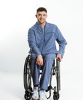 A man wearing a blue scrub set sits in a wheelchair against a plain white studio background.