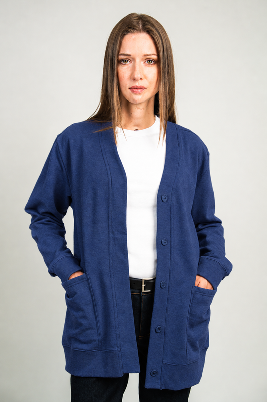A woman modeling a navy blue open-front cardigan with large front pockets over a white top and black pants, photographed against a plain light gray studio background.