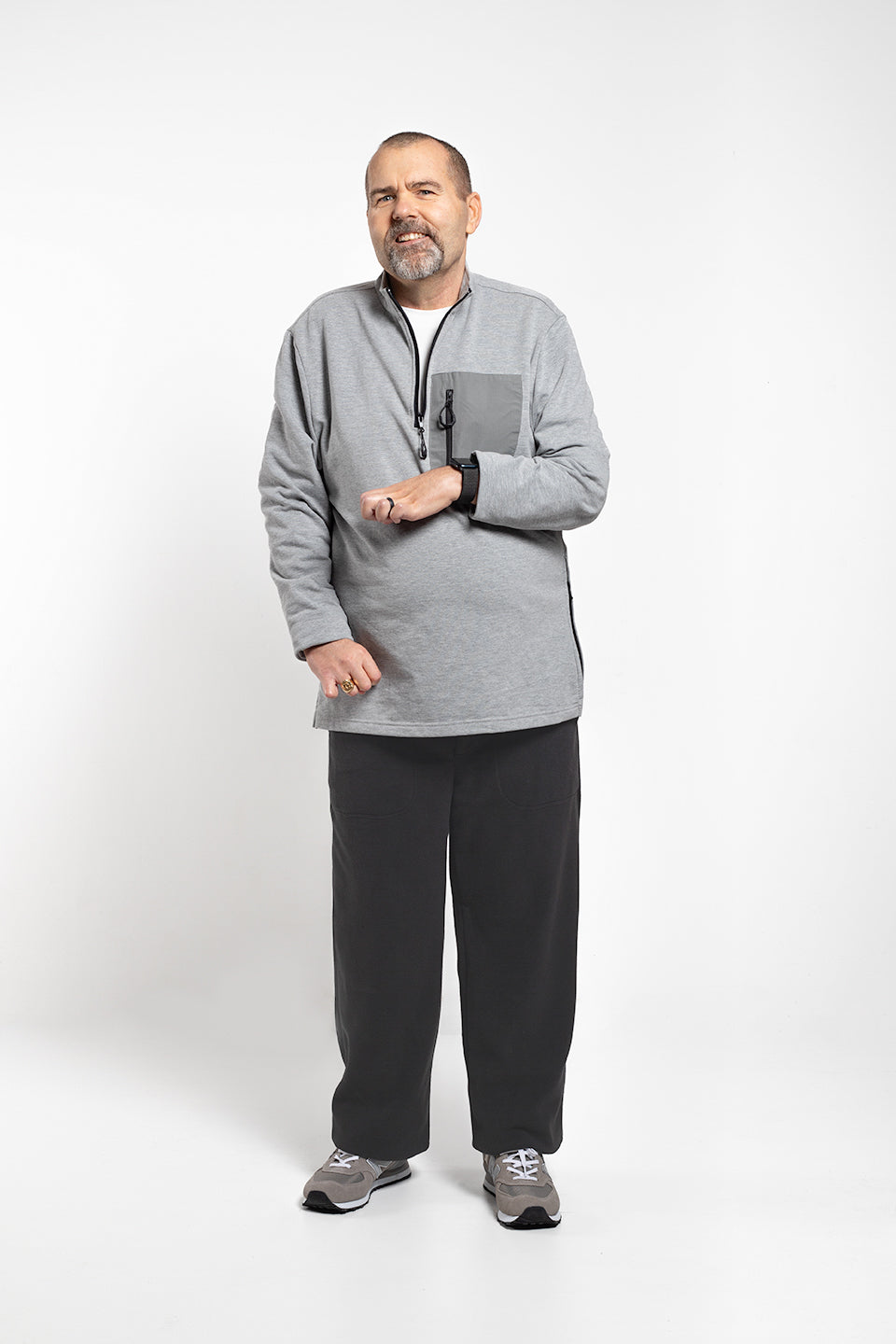 A man wearing a heather gray quarter-zip fleece pullover, black sweatpants, and gray athletic shoes, standing against a light gray studio background.