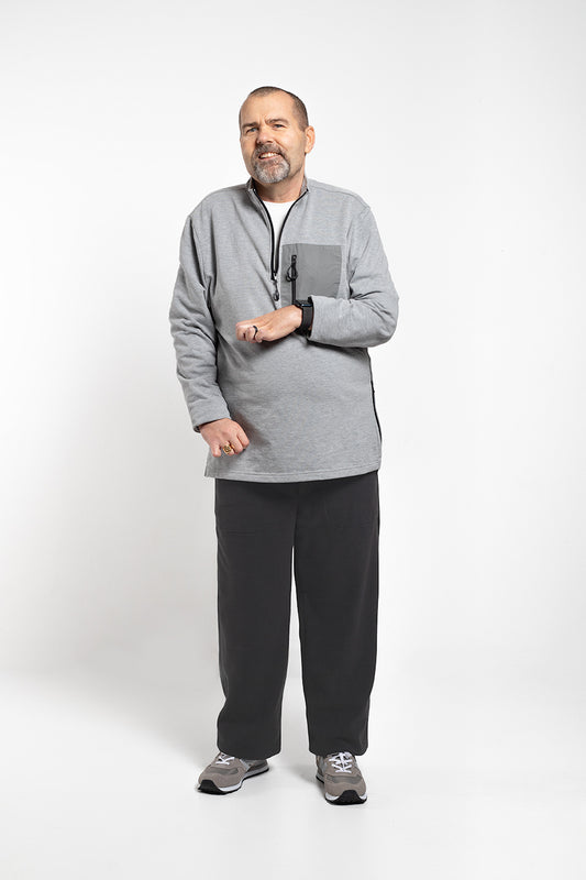 A man wearing a heather gray quarter-zip fleece pullover, black sweatpants, and gray athletic shoes, standing against a light gray studio background.